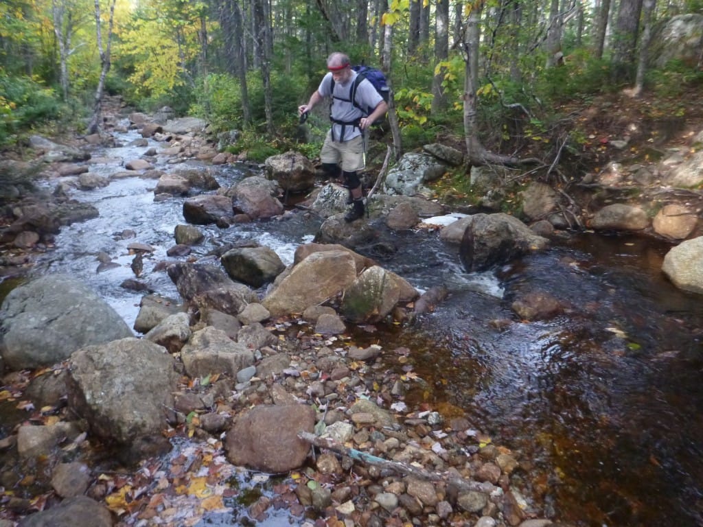 A hiker crosses a rocky stream.