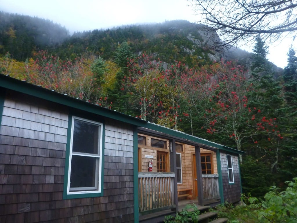 A building with wooden shingles sits nestled in a foggy green forest.