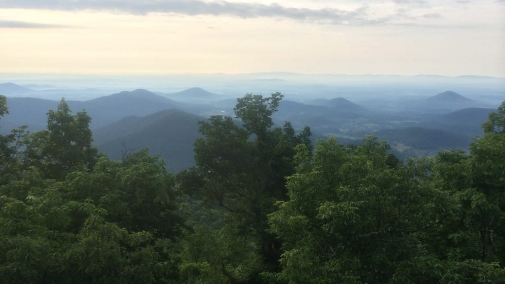 An early sunset illuminates trees and distant mountains from this overlook.