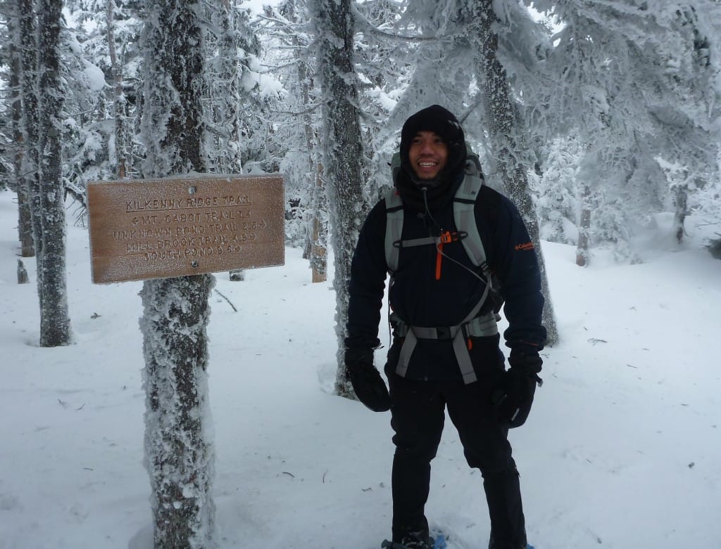 A hiker stands next to a trail sign in a snowy forest.