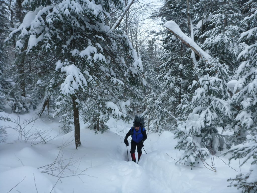 A hiker climbs a slope through deep snow.