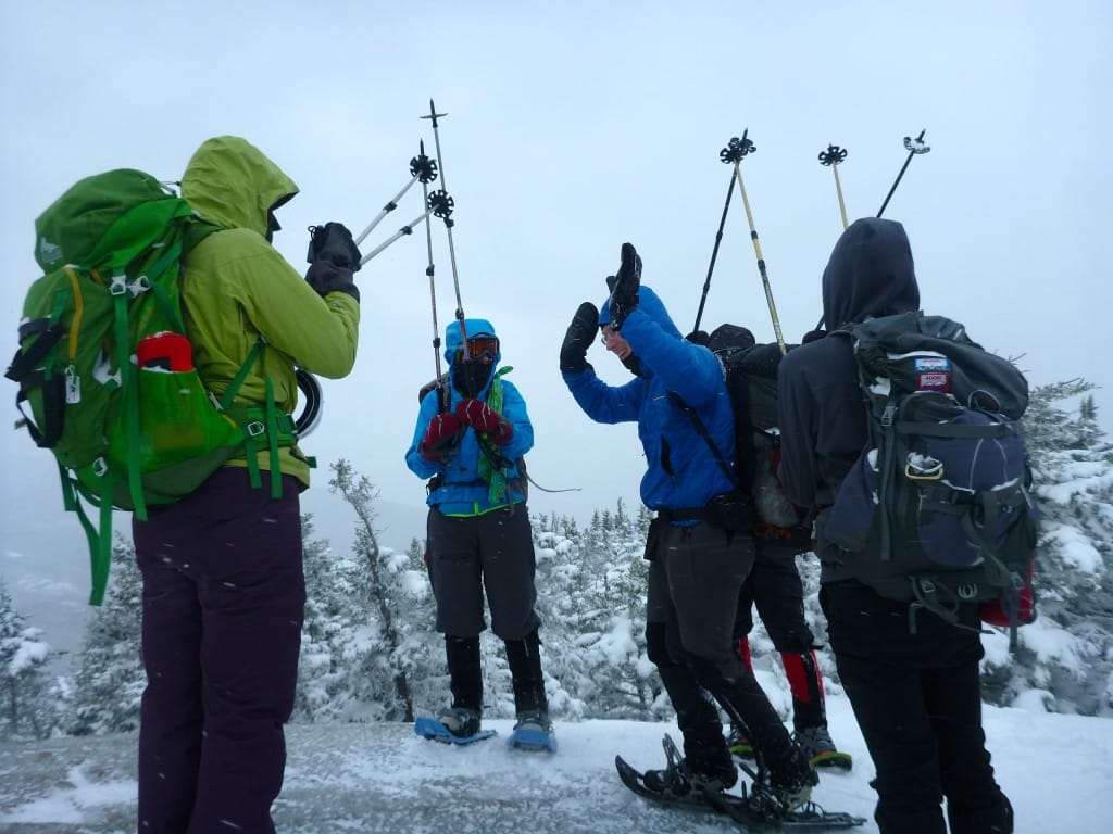 A group of hikers stand on a snowy summit and celebrate.