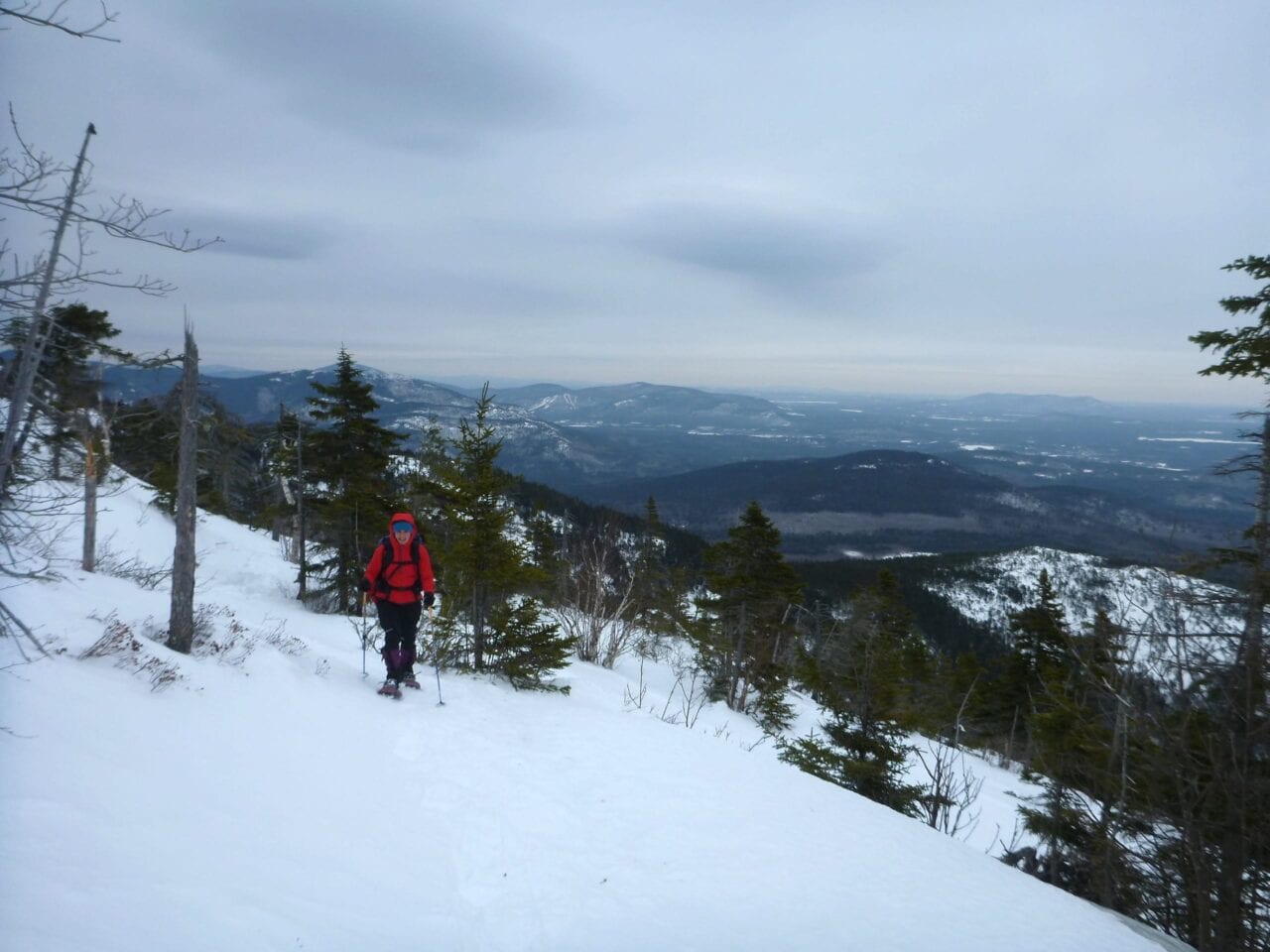 A hiker climbs up a snowy slope with a valley visible in the background.