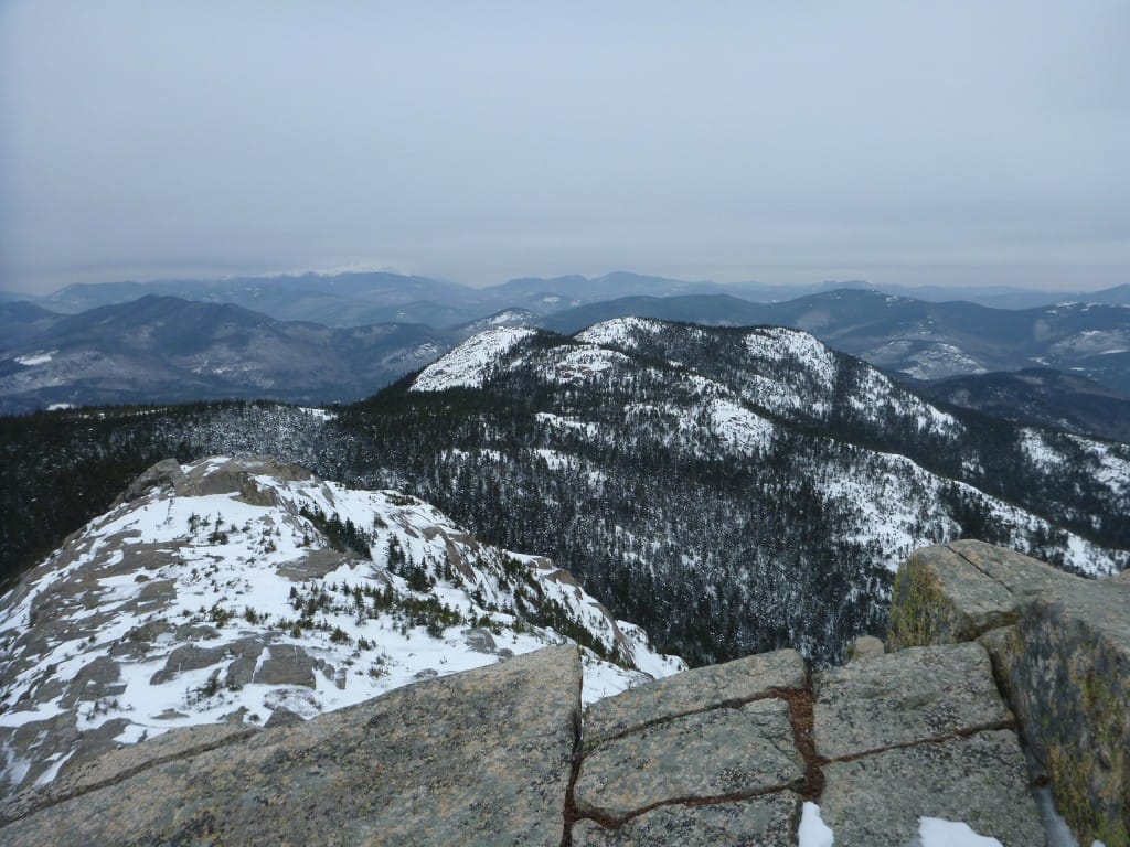 A view from a rocky cliff shows distant snowy mountains.