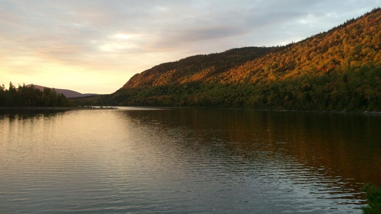 A sunset illuminates a calm lake surrounded by low mountains.