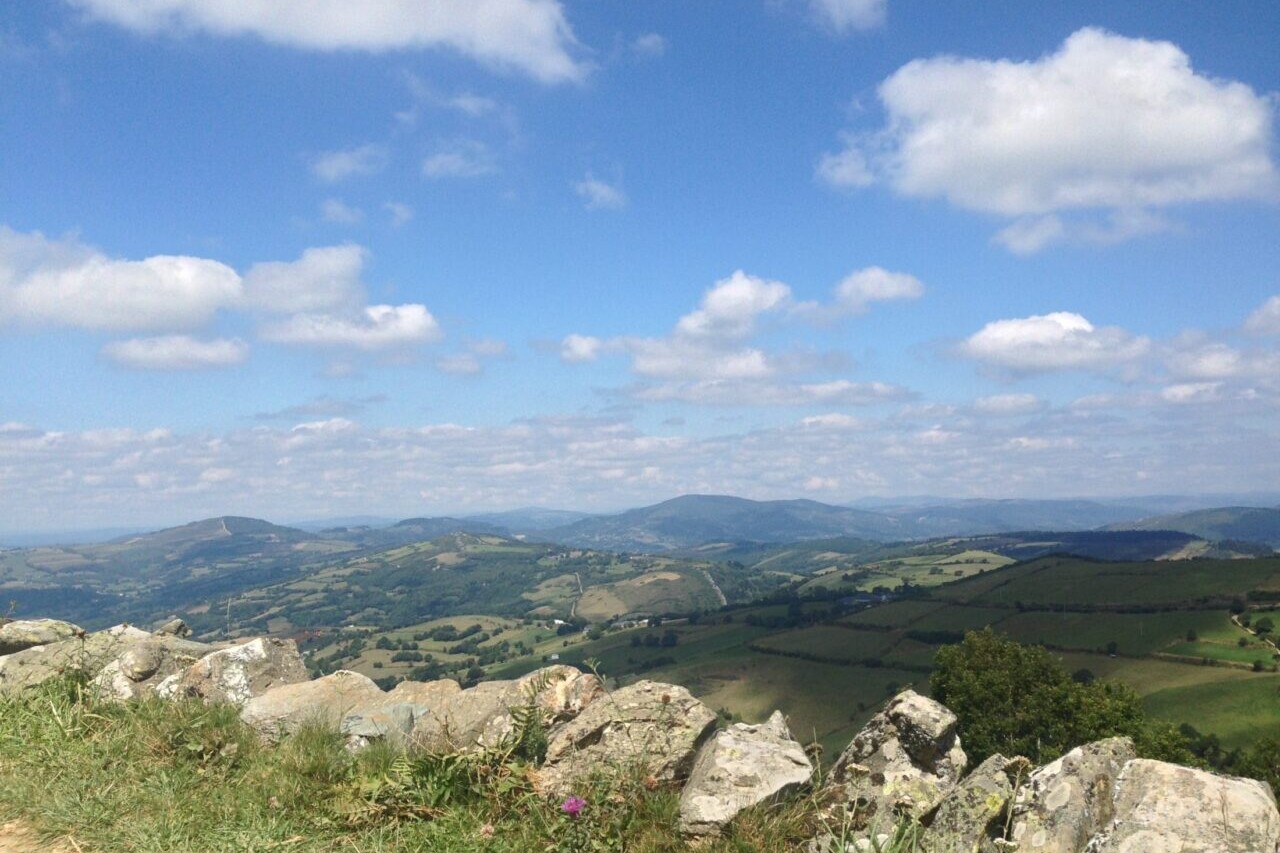 A trail looks over a rock wall to distant mountains and blue skies.