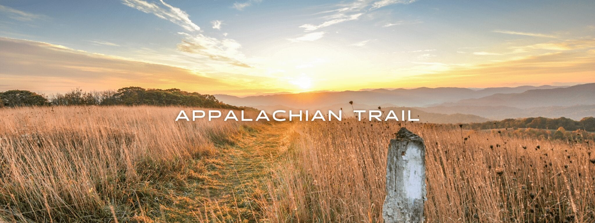 A white blaze and a trail appear through brown grass on top of a hill during sunset on the Appalachian Trail