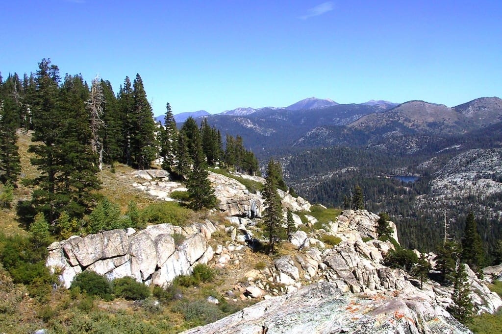 A rocky ridge and meadows overlook distant rocky mountains.