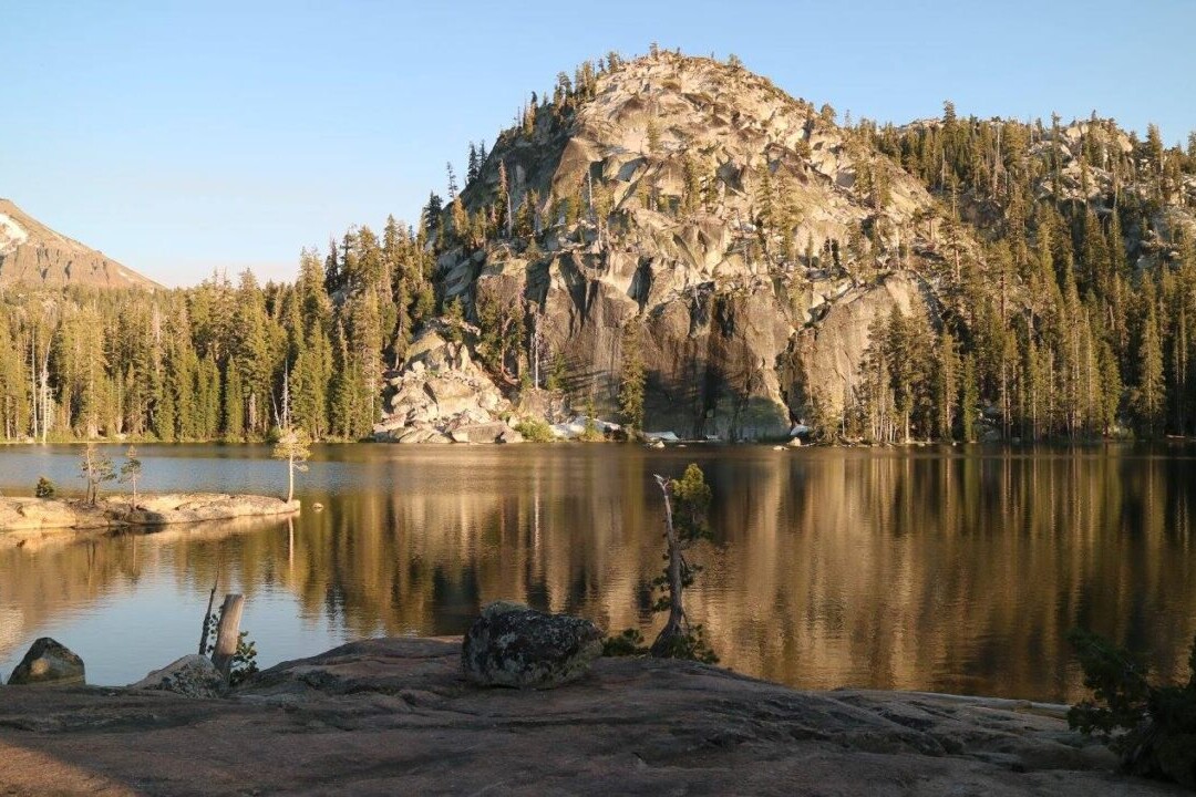 A lake reflects a nearby mountain and trees.