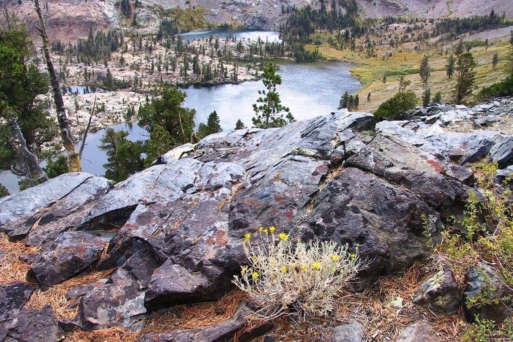 A rocky view overlooks a blue lake and meadows.