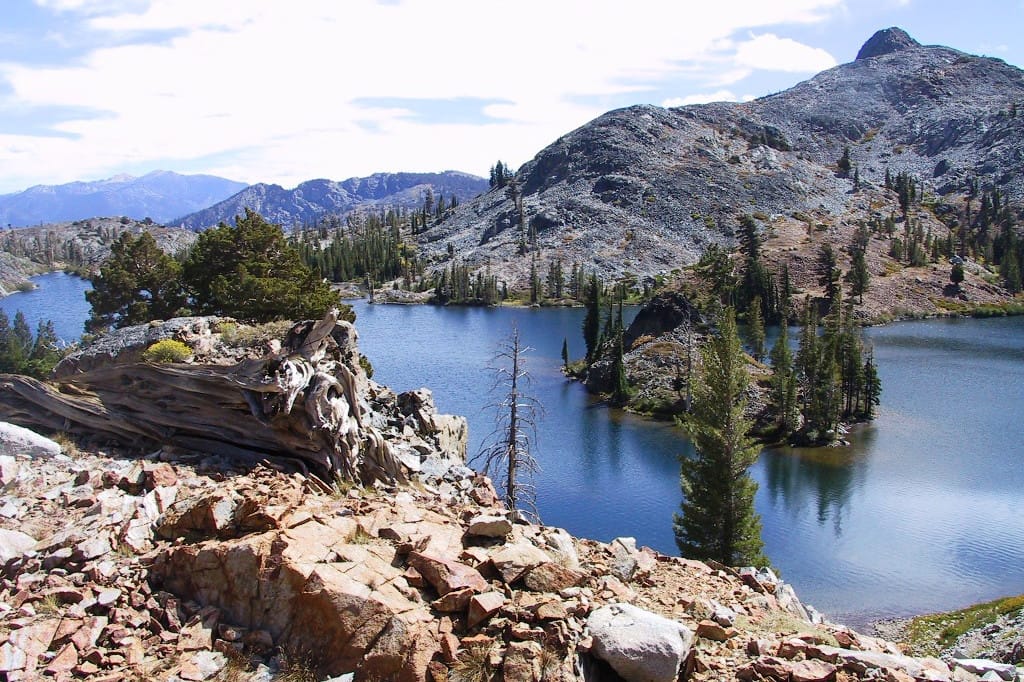 A rocky view overlooks a blue lake and mountains.