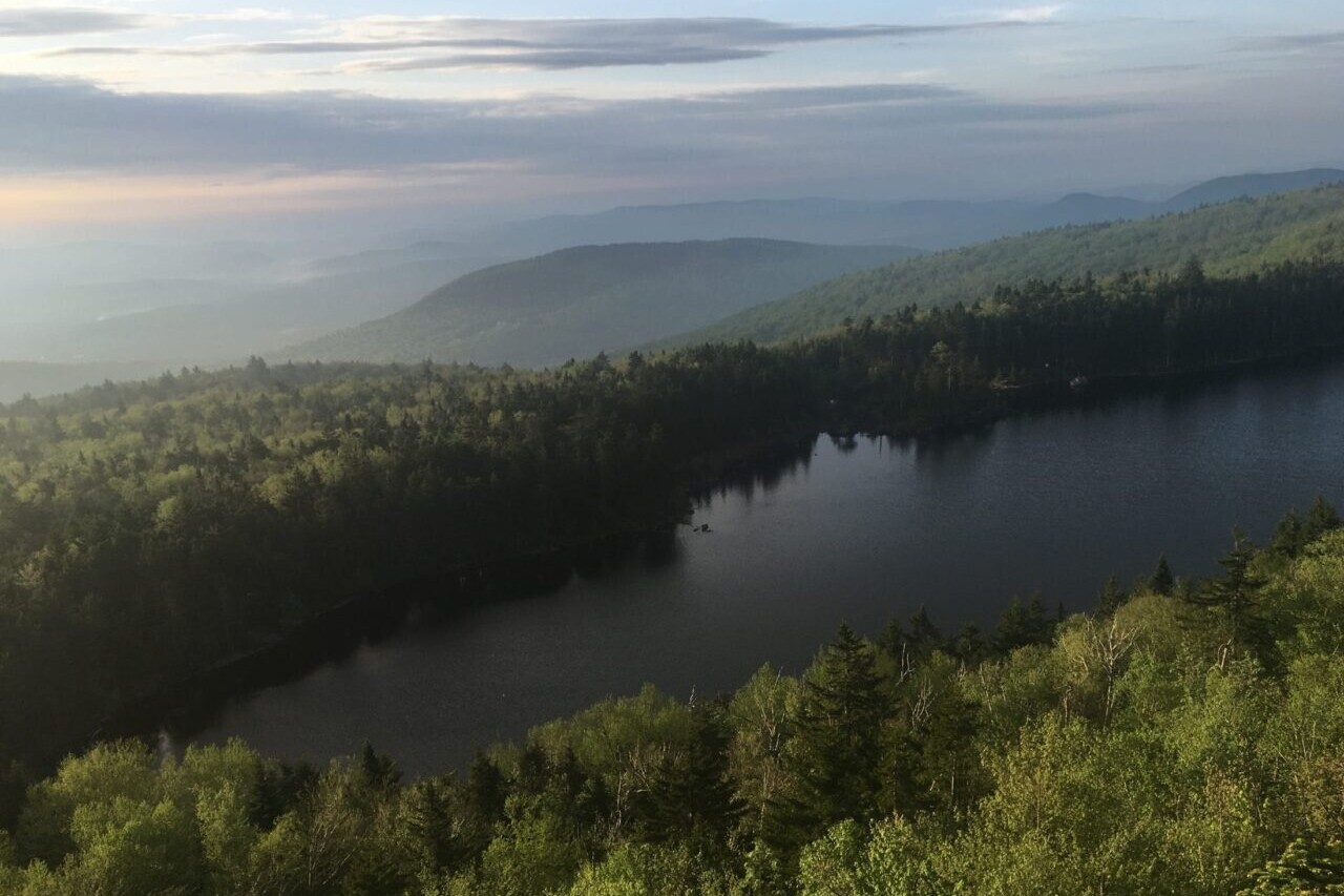 A view shows a clear lake reflecting the forest surrounding it.