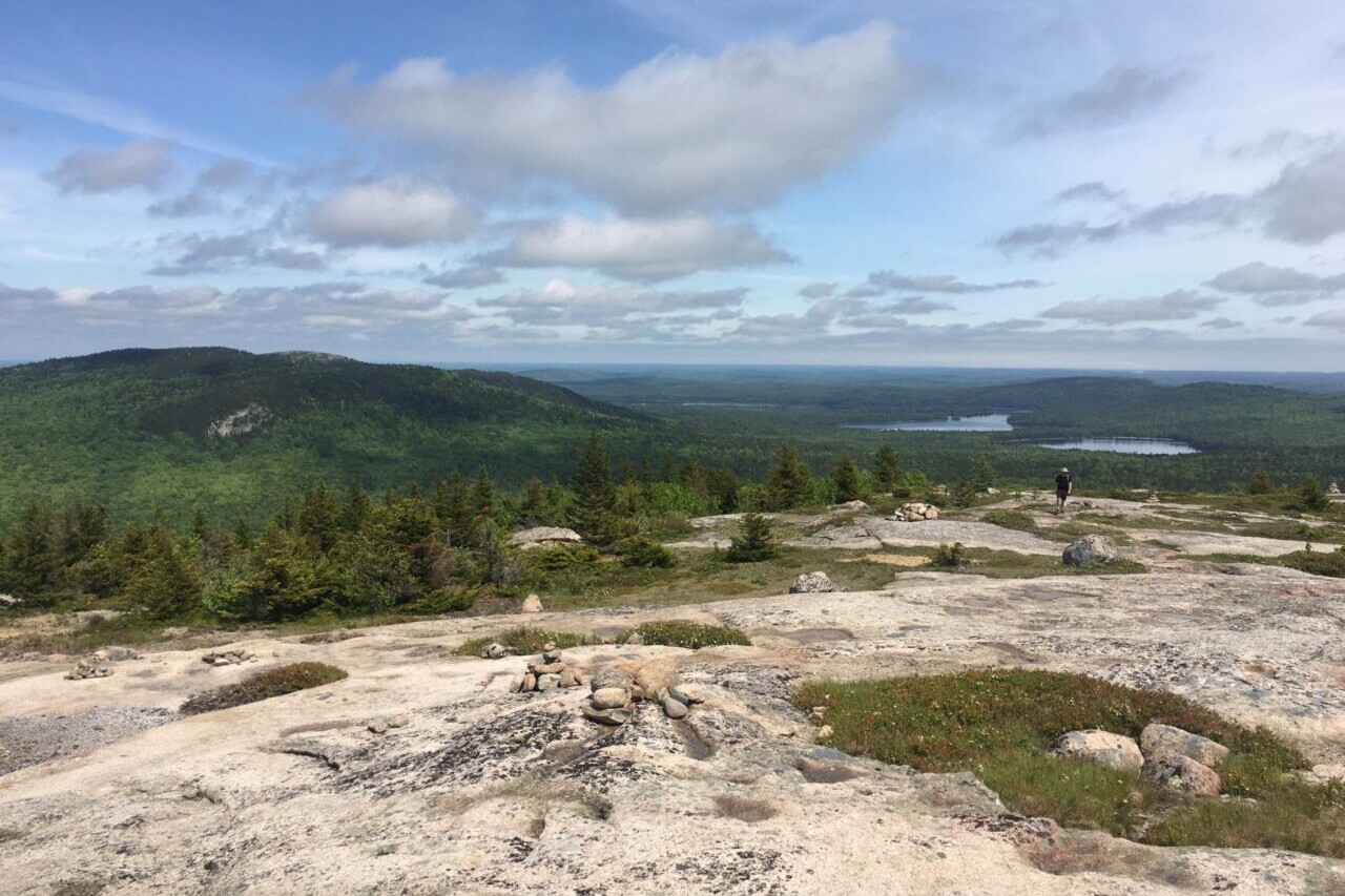A rocky ridge overlooks a green valley and distant lakes.
