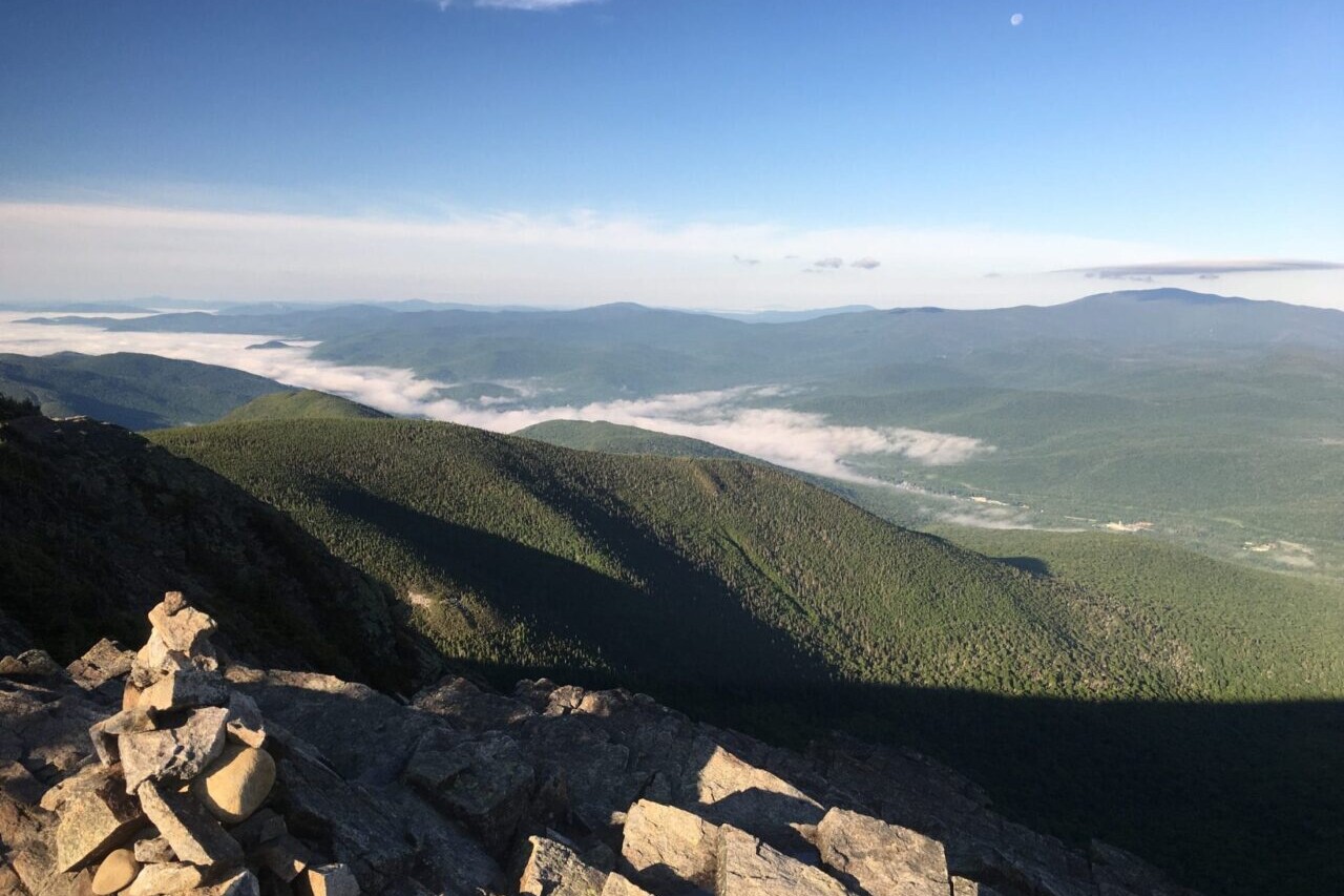 A rocky ridge overlooks a green valley and distant mountains.