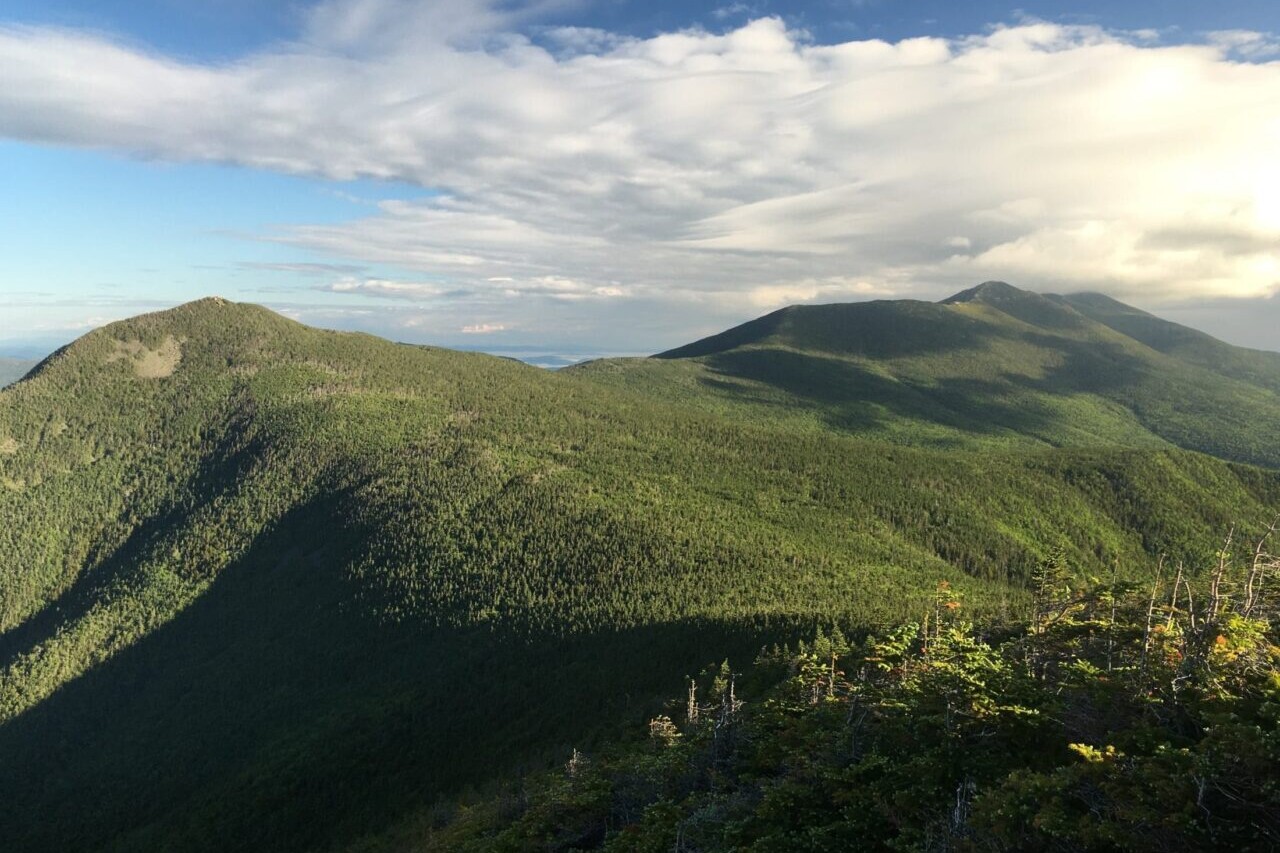 A green ridge meanders into the distance towards clouds and blue sky.