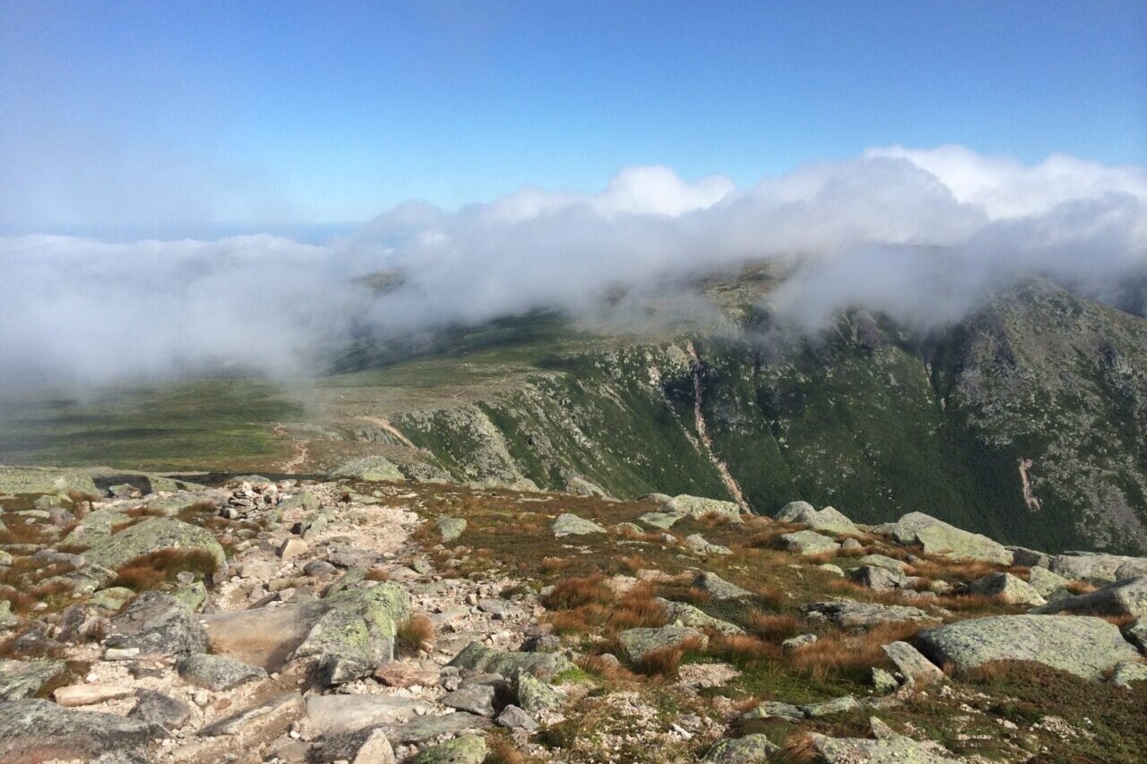 A rocky ridge is covered in low clouds and a blue sky.
