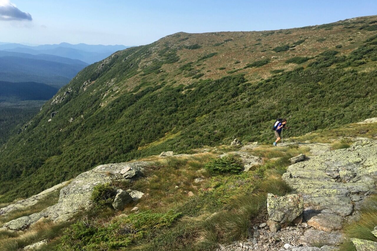A hiker ascends to a ridge overlooking distant mountains.