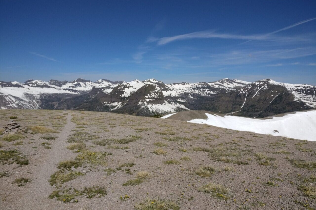 A trail meanders through a dusty field towards distant snowy mountains.