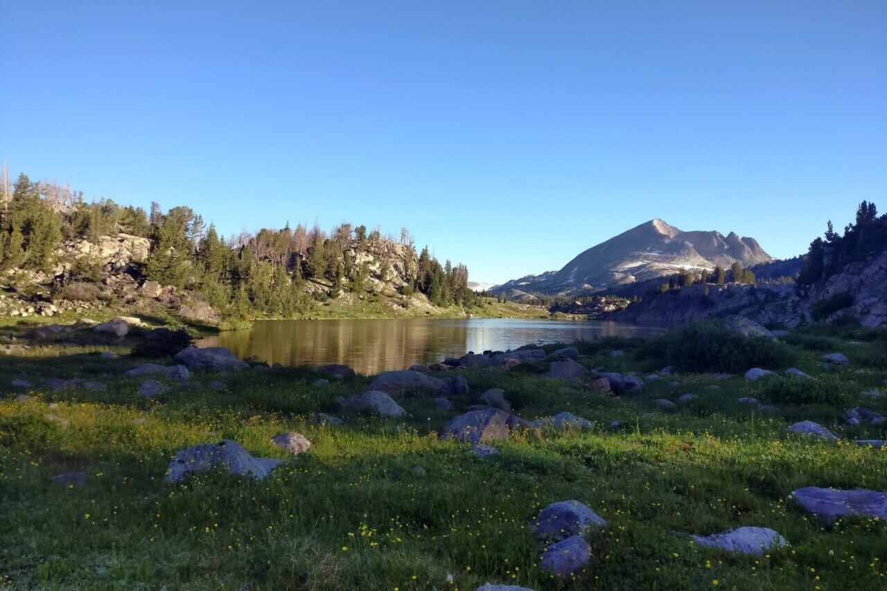 A lake sits in a green field in front of distant mountains.