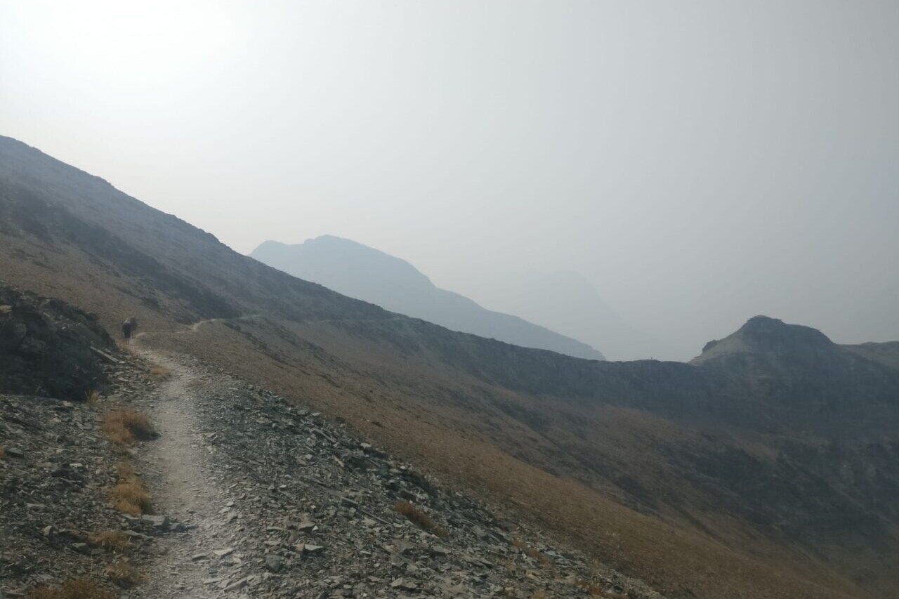 A trail travels along a rocky mountainside towards misty mountains.