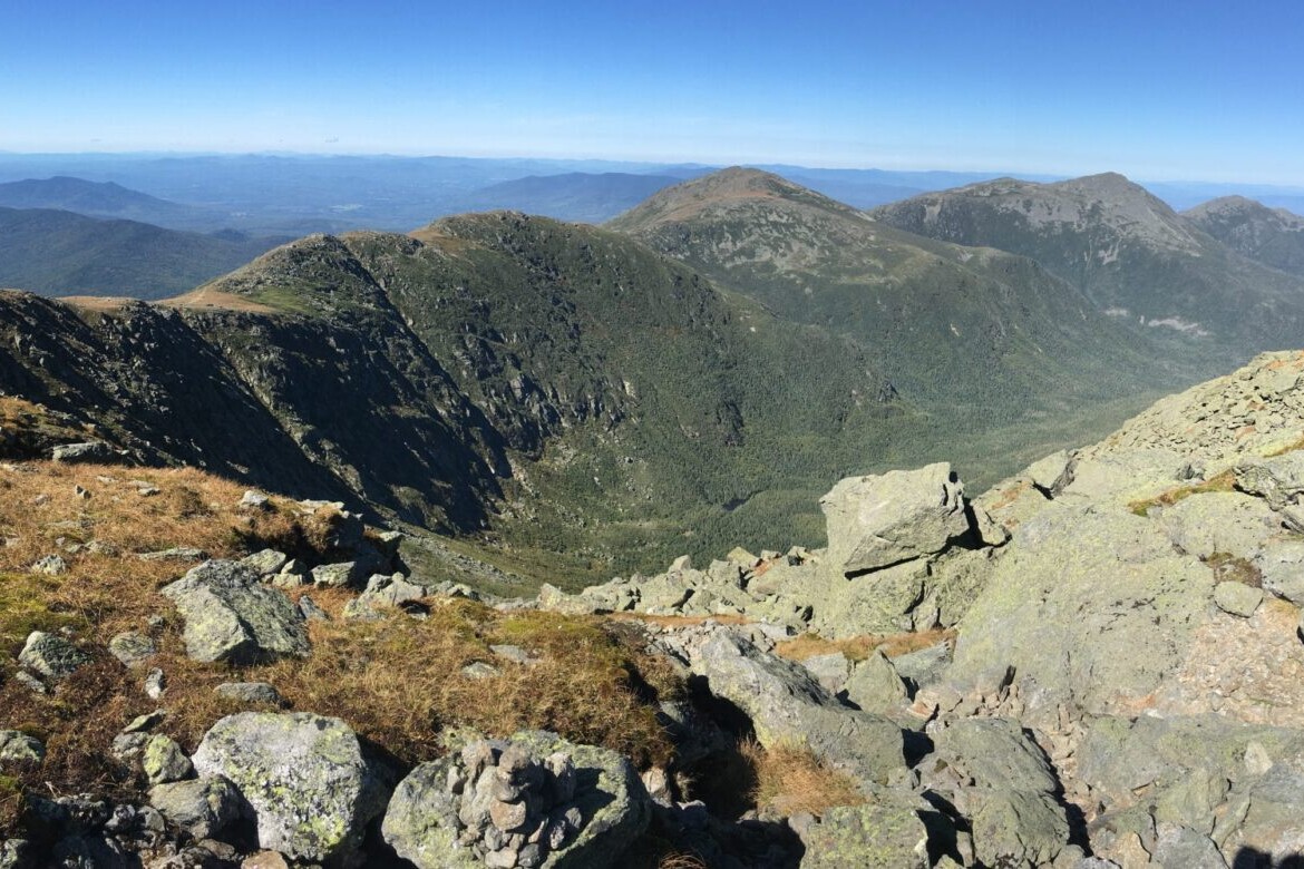 A rocky ridge meanders towards distant mountains and a blue sky.