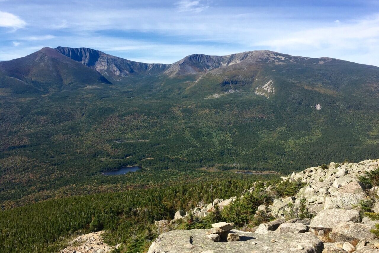 A rocky ridge overlooks a green valley and distant mountains.