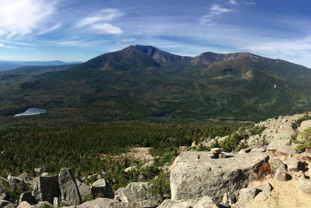 A rocky ridge overlooks a green valley and distant mountains.