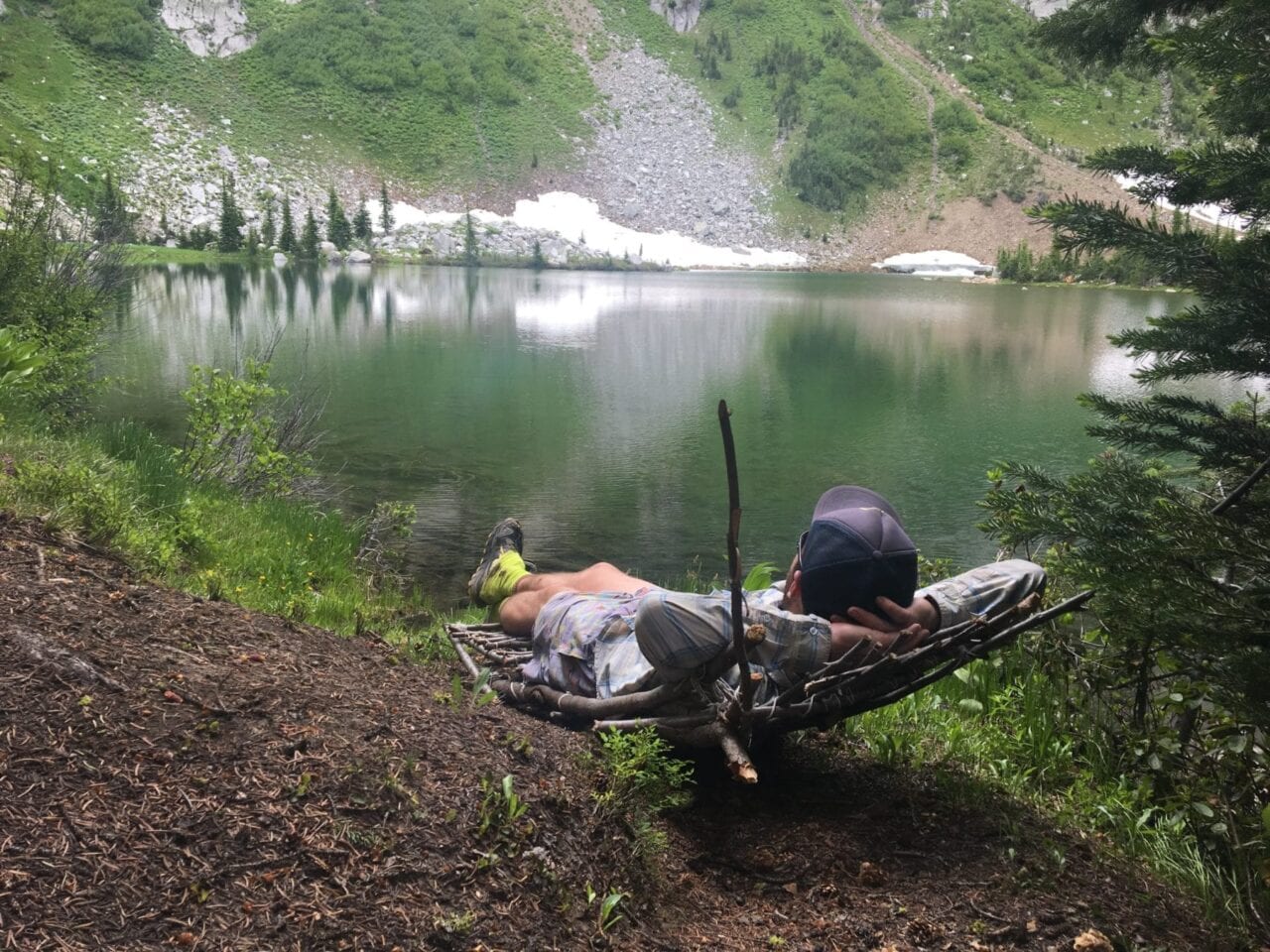 A hiker lounges by a green lake.