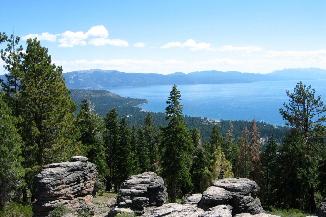 A rocky view overlooks a blue lake and meadows.