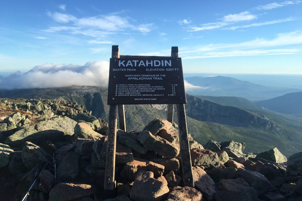 The summit sign for Mount Katahdin is silhouetted against a blue sky.
