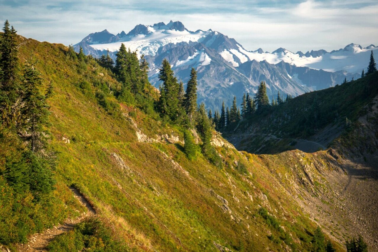 A trail leads along a golden ridge towards distant snowy mountains.