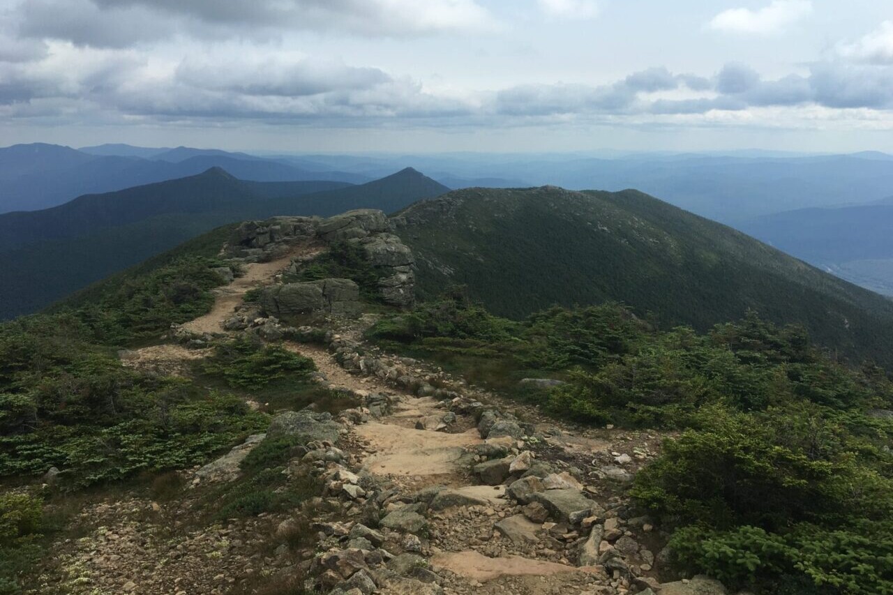 A rocky path leads along a ridgeline toward distant mountains.