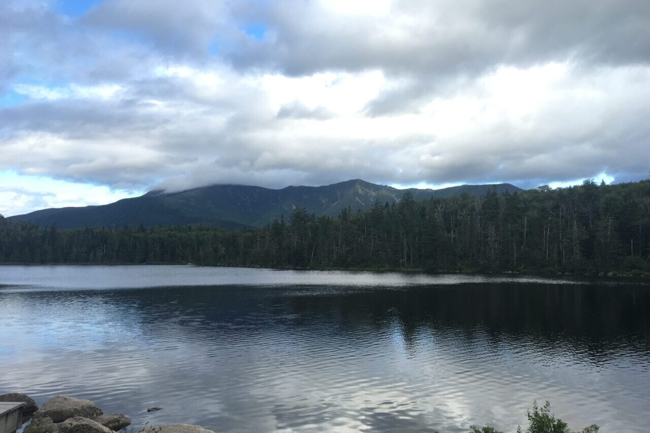 A reflective lake shows mountains and forests in the background.