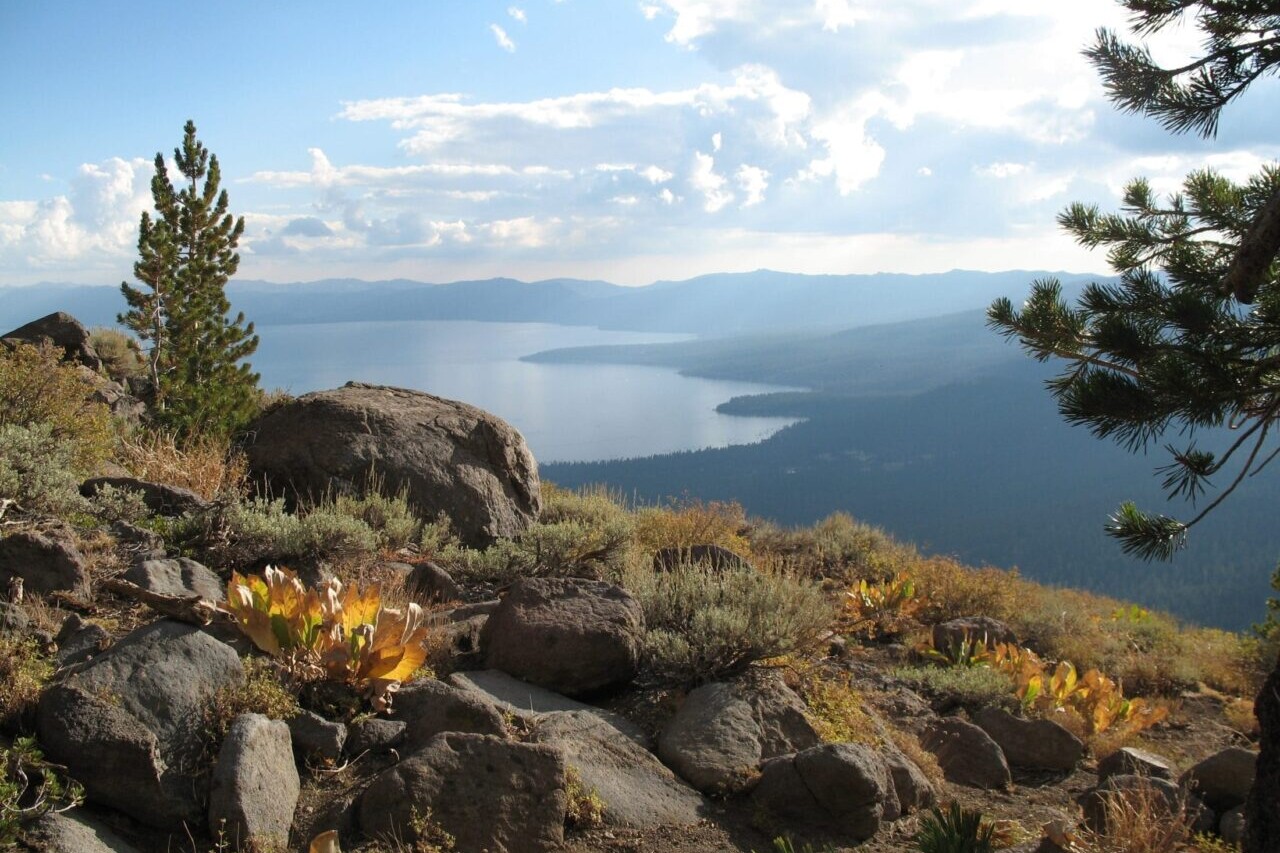 A rocky view overlooks a blue lake and meadows.