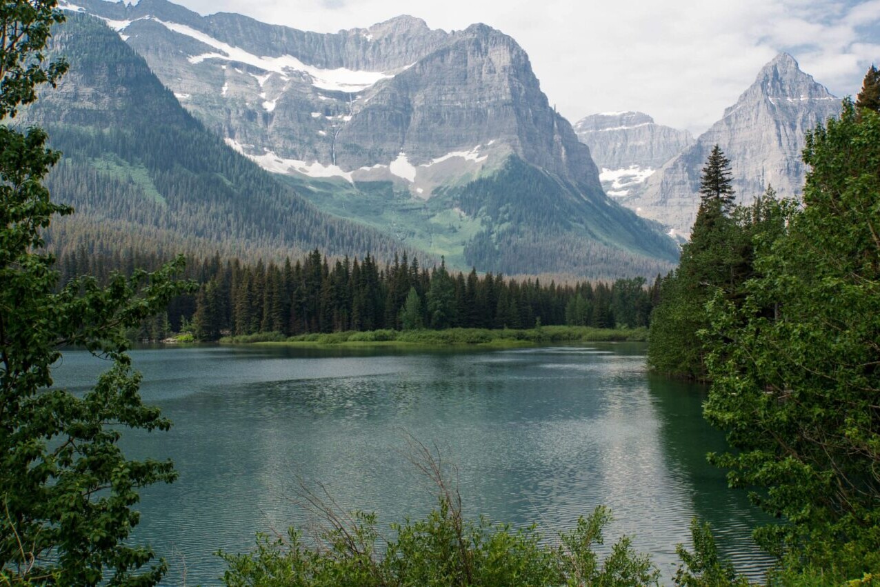 A blue lake sits in front of tall snowy mountains.