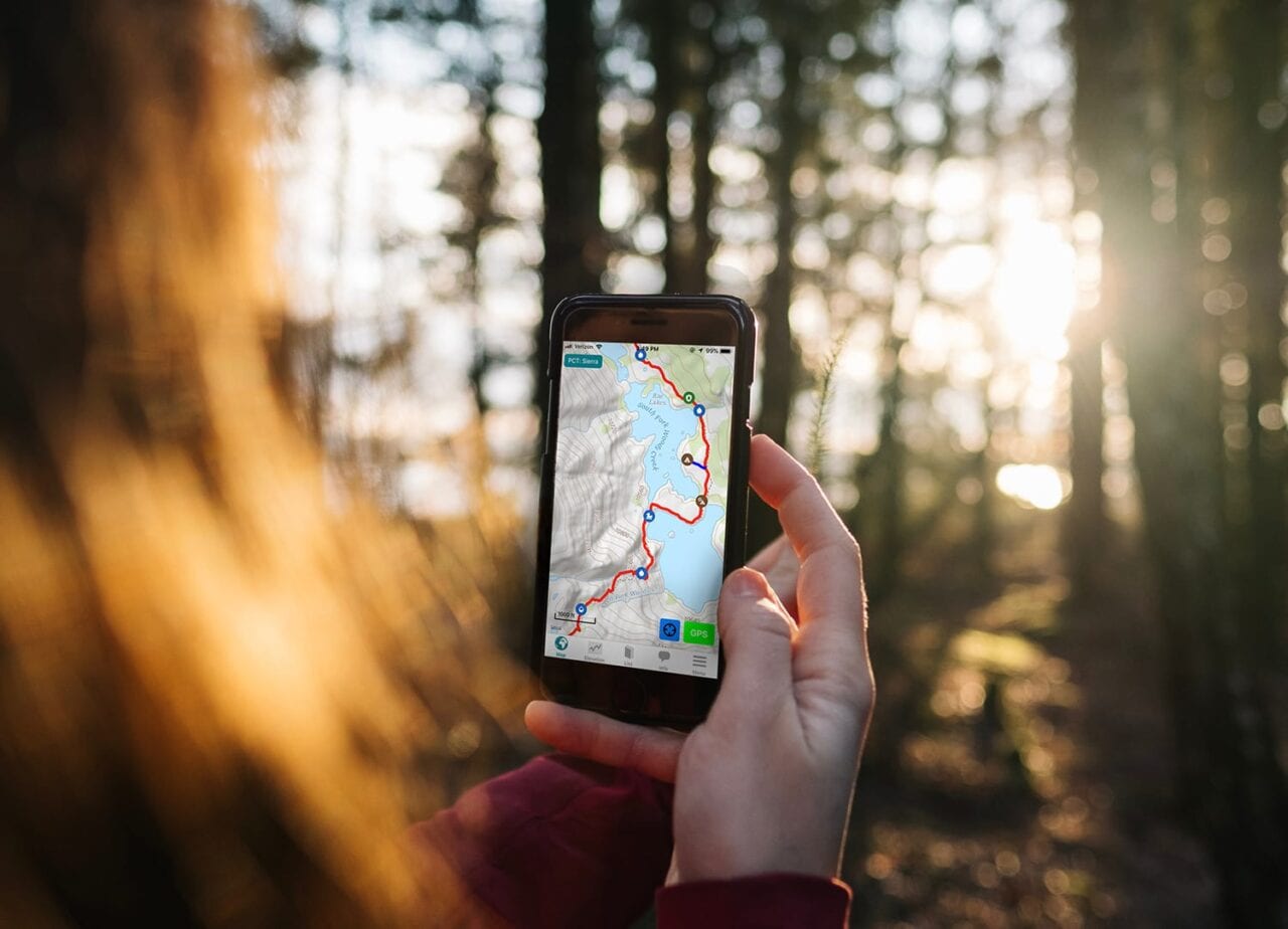 A woman holds a phone showing the Guthook Guides trail guide app.