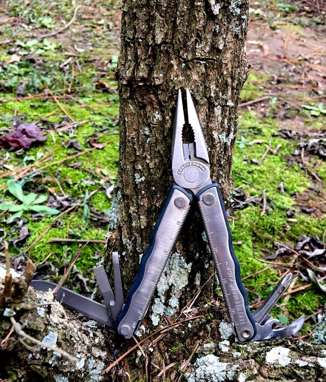An open multi-tool sits against a tree.