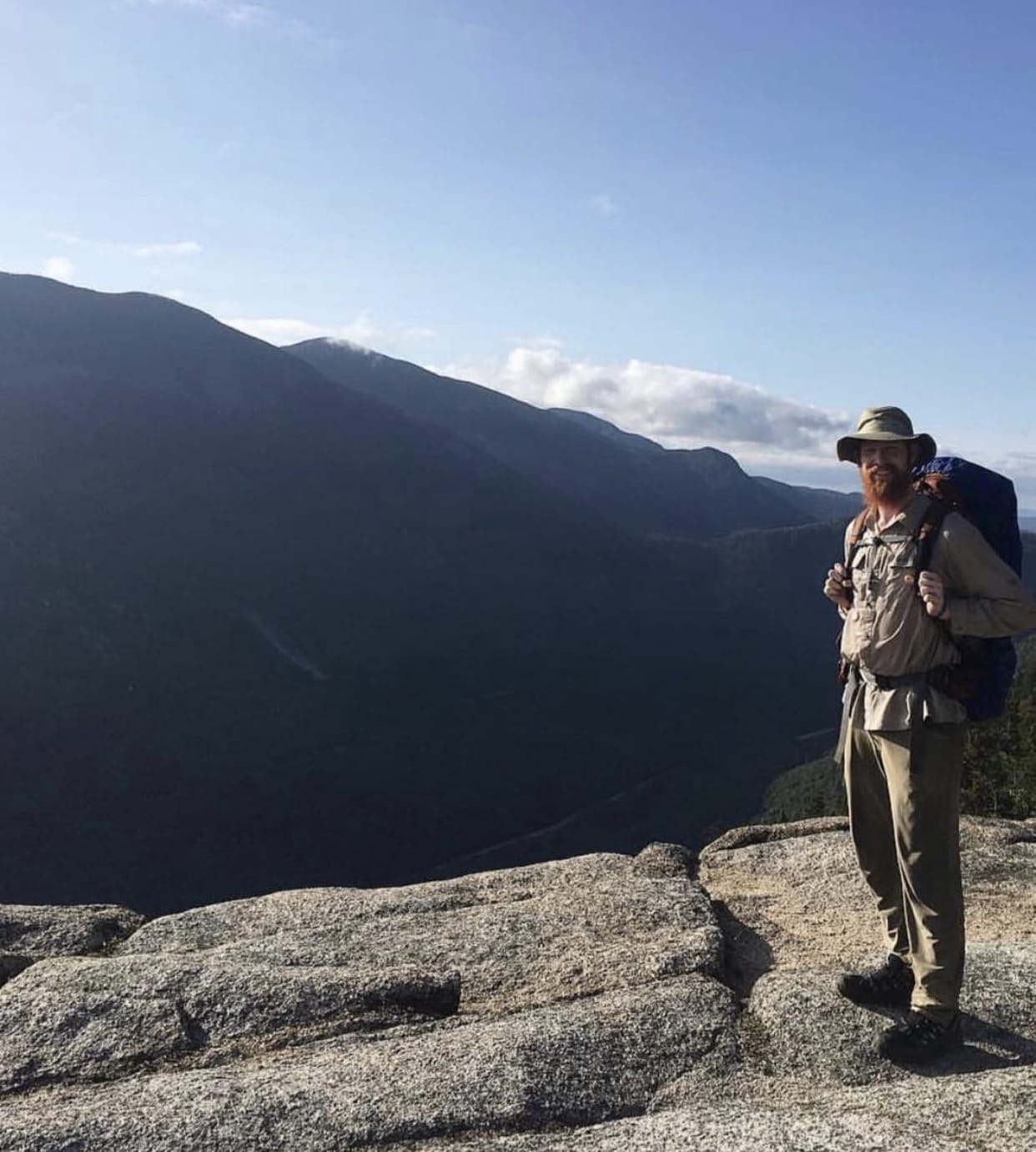 A thru hiker standing with a mountain in the background.
