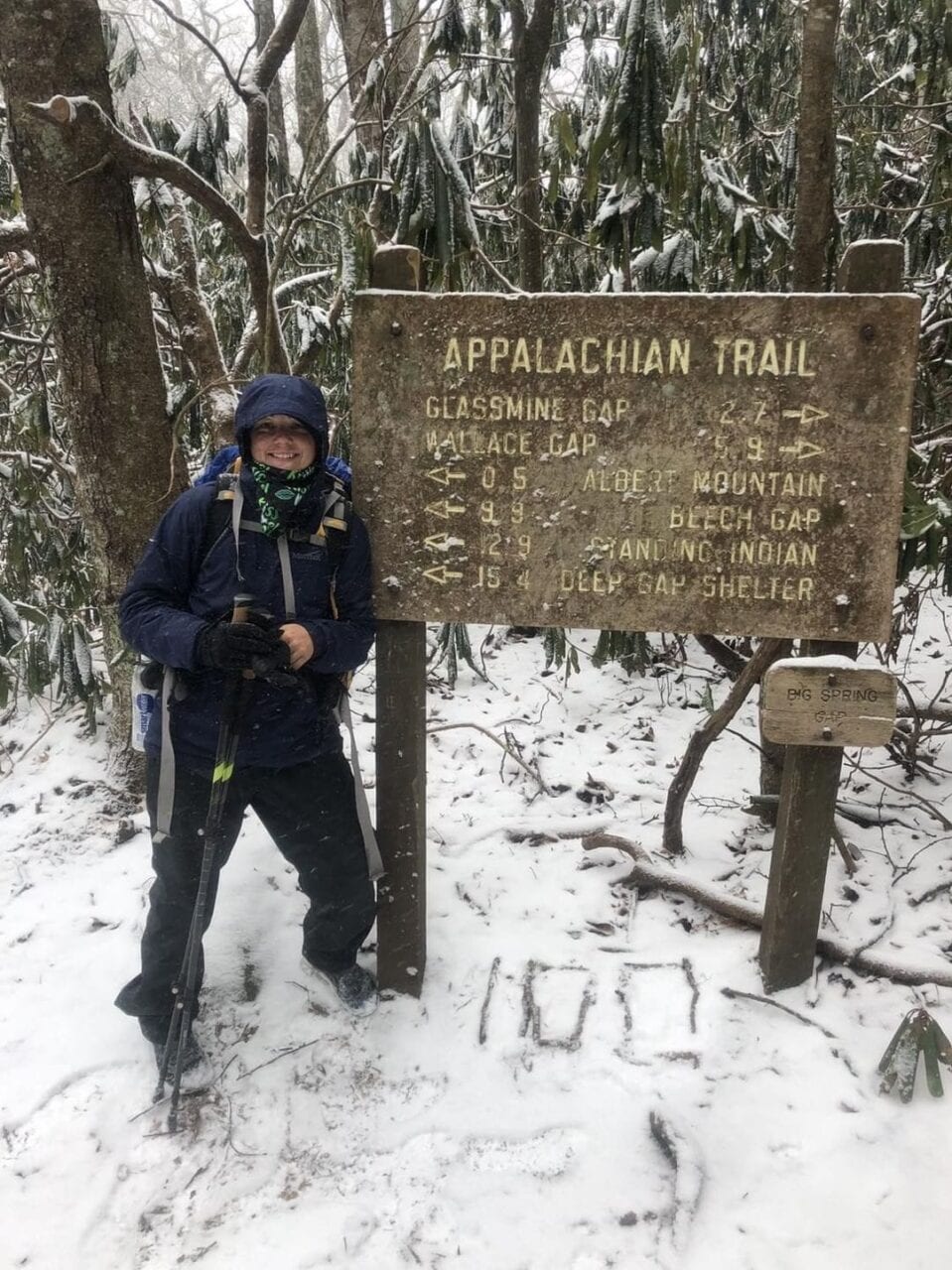 A hiker next to an Appalachian Trail sign in the snow.