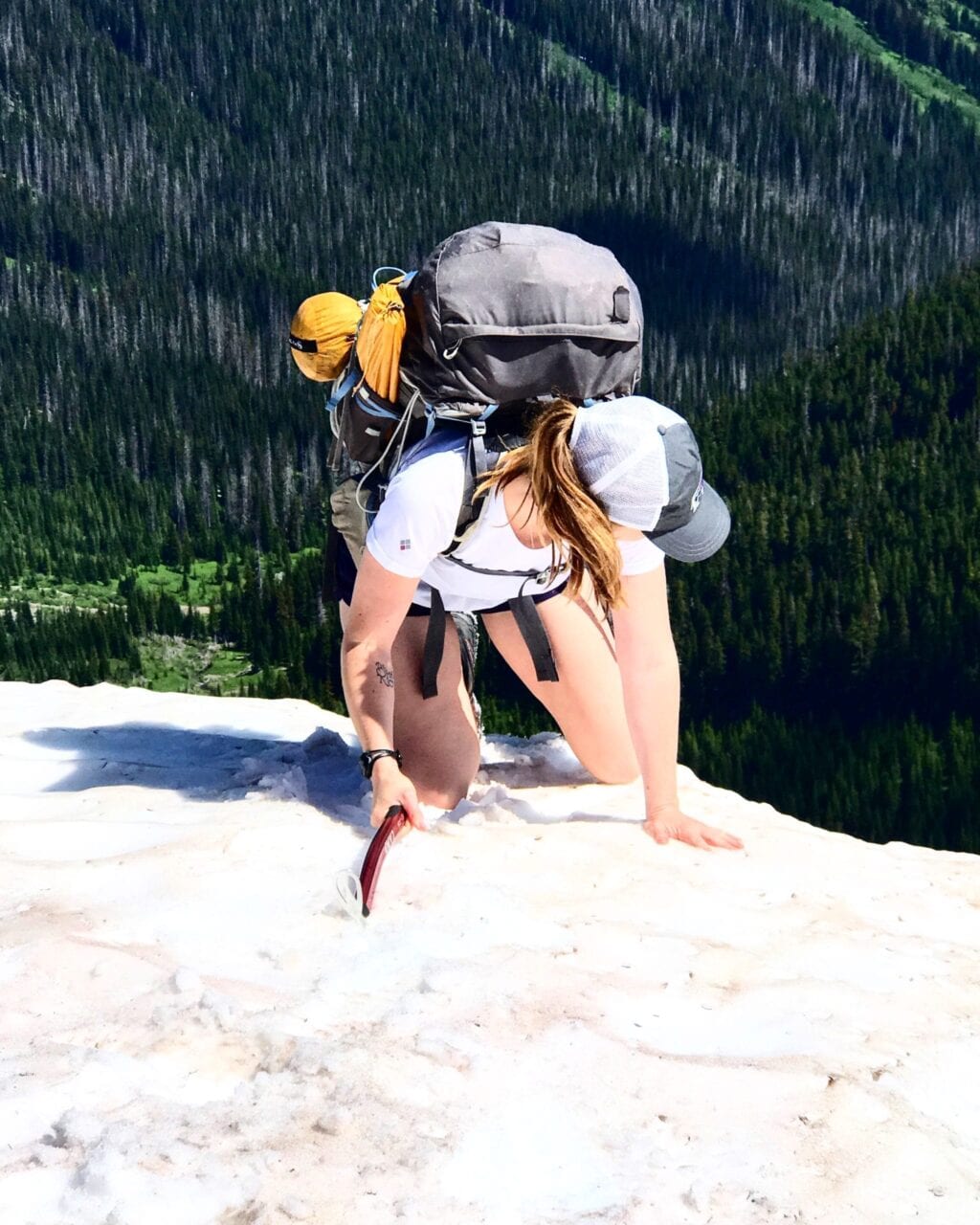 A woman with a backpack climbs up a snowy mountain.