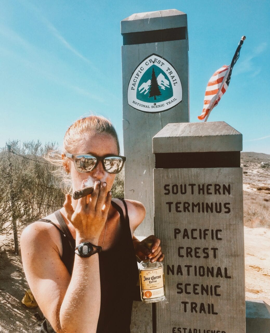 A woman stands with a cigar next to the southern terminus monument of the Pacific Crest Trail.