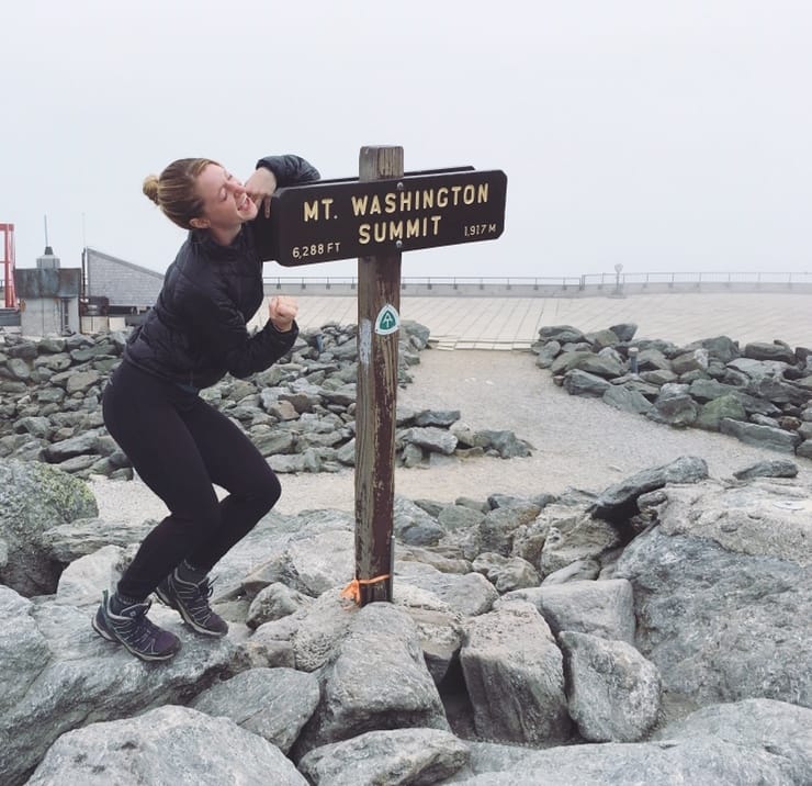 A woman poses next to the Mount Washington Summit sign.