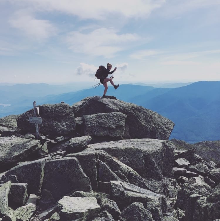 A hiker with a backpack poses on top of a rock pile.
