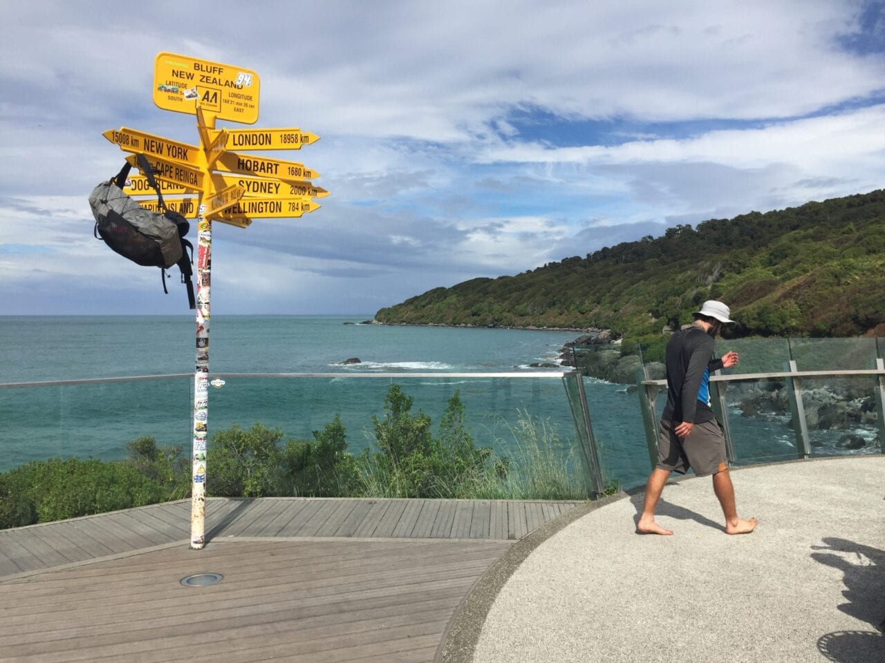 A man walks away from the Te Araroa sign that has his backpack hanging on it.