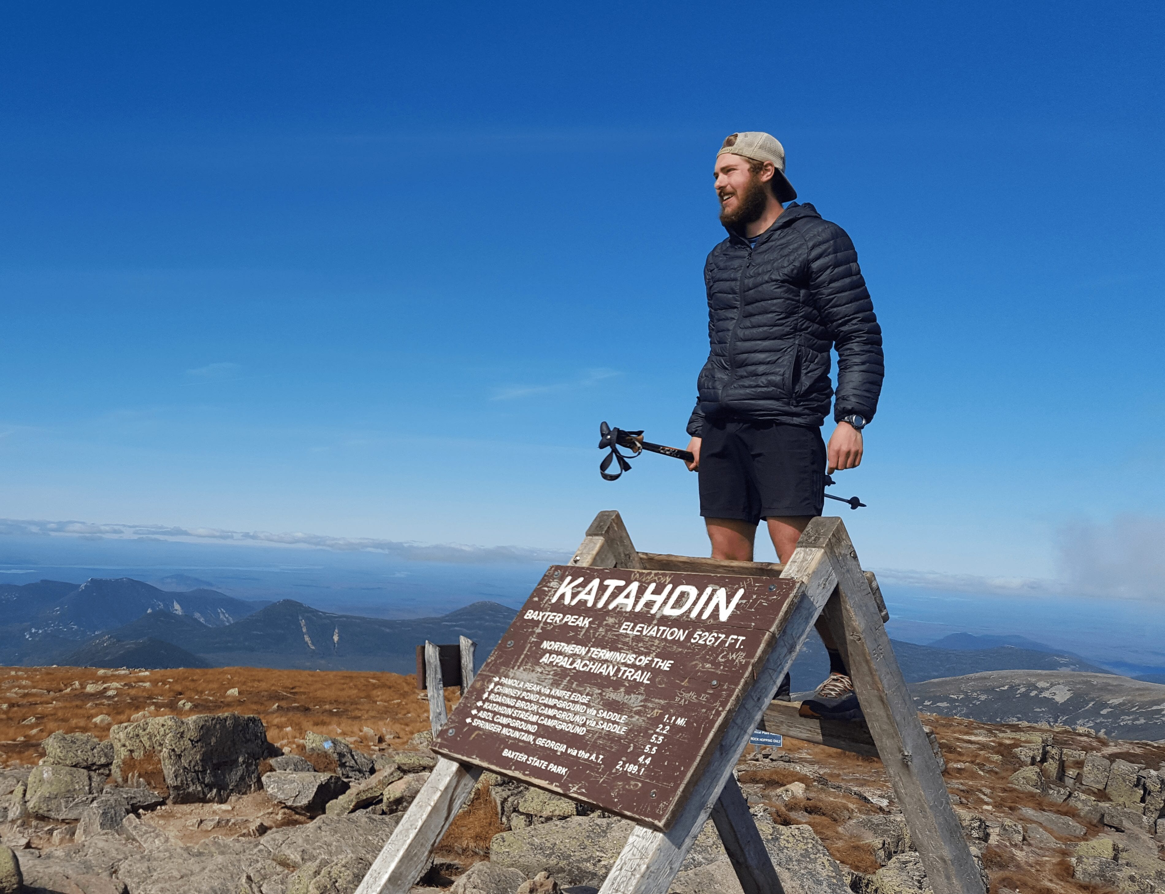 A hiker stands on top of the Mount Katahdin sign on the Appalachian Trail.