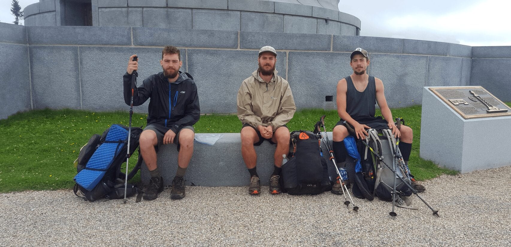 A group of guys hiking the Appalachian Trail sit on a bench with their backpacks.