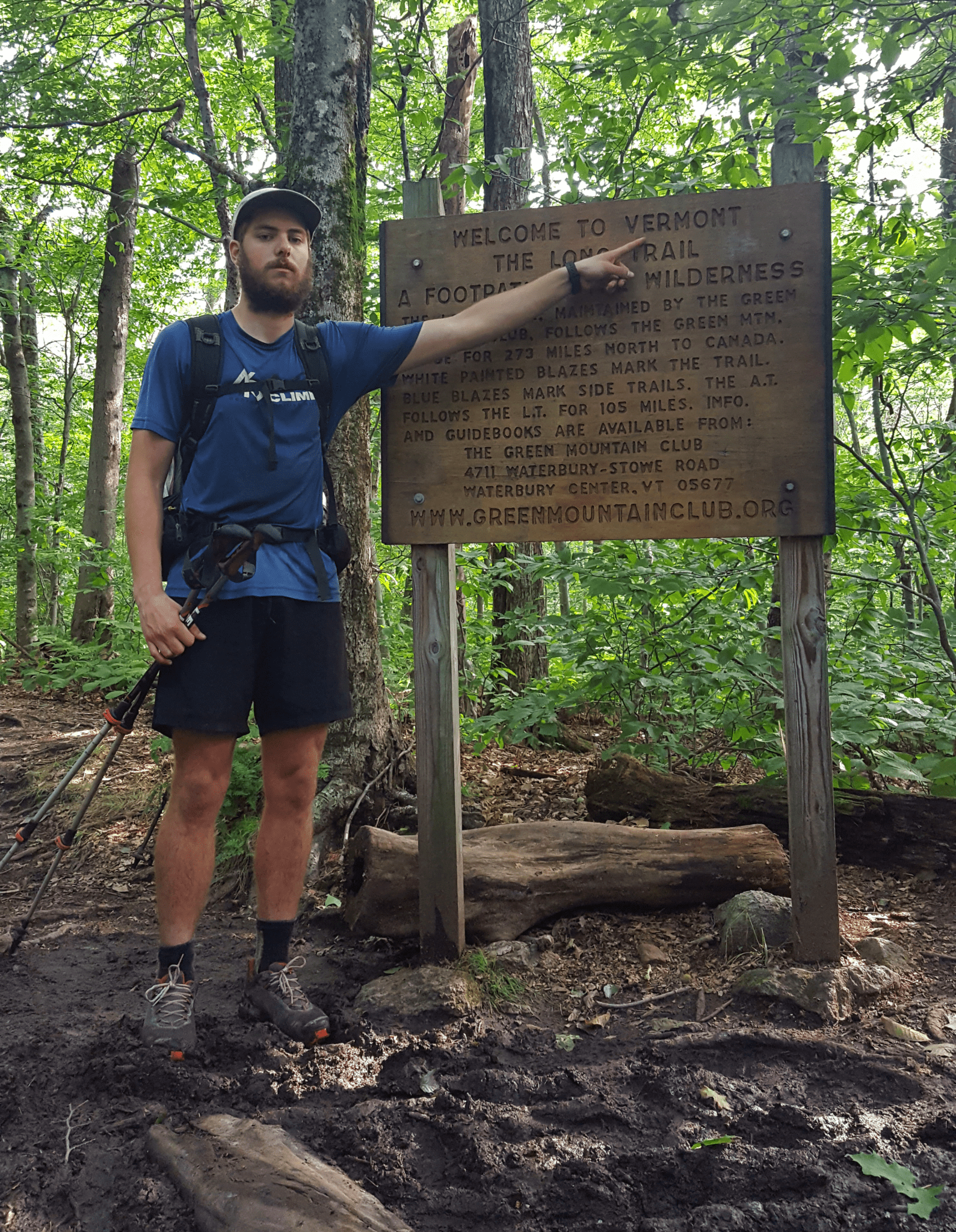 A hiker stands in the woods pointing at an Appalchian Trail sign.