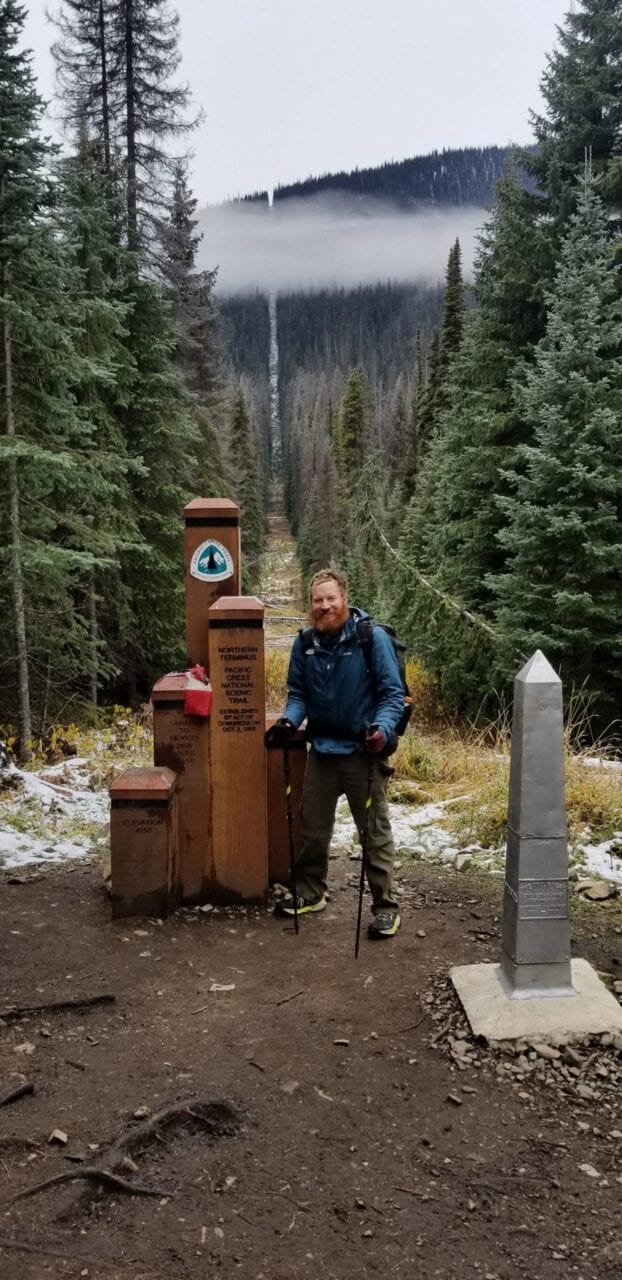 A man stands next to the northern terminus of the Pacific Crest Trail.