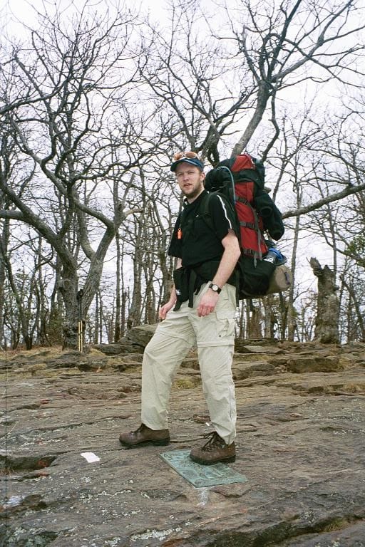 A hiker stands on a a slab of rock with a backpack on.