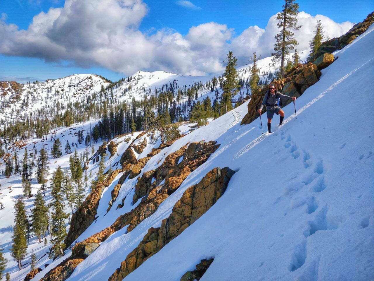 A hiker standing on the side of a mountain in the snow.